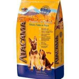 Saco de alimento Atacama Puppies All Breeds para cachorros de todas las razas, con envase amarillo y azul, imágenes de dos perros y beneficios nutricionales destacados en el empaque.